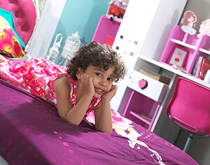 mor renkli yatağa yüz üstü yatan pembe giysili kız çocuğu